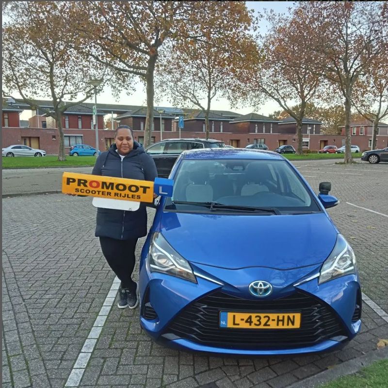 Geslaagde leerling met het lesbord naast de blauwe lesauto van Autorijschool Promoot