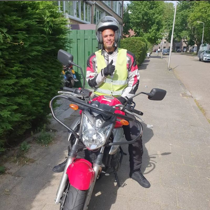 Geslaagde motorleerling met duim omhoog op de rode lesmotor van Autorijschool Promoot