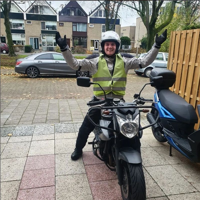Geslaagde motorleerling met de armen omhoog op de rode lesmotor van Autorijschool Promoot