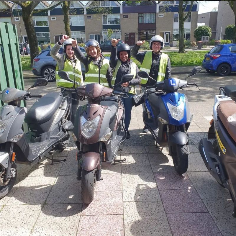 Vier scooterleerlingen juichen naast de lesscooters