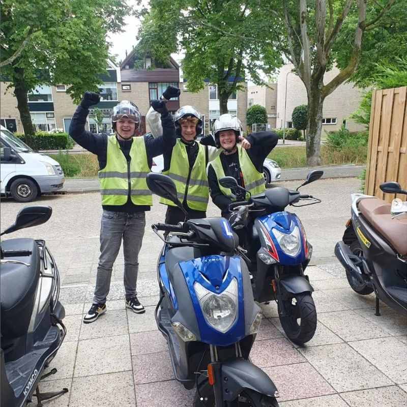 Drie scooterleerlingen van Autorijschool Promoot juichen naast hun lesscooters in Ridderkerk